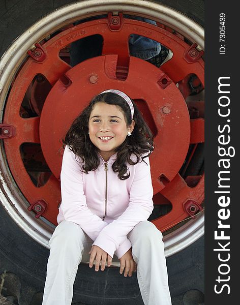 Little girl setting in the wheel of a big red tractor. Little girl setting in the wheel of a big red tractor