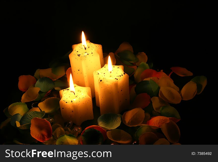 Three candles and petals with warm and magic light in black background