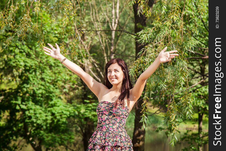 Young beautiful smiling girl holds out her hands to the sky in the park on summer day