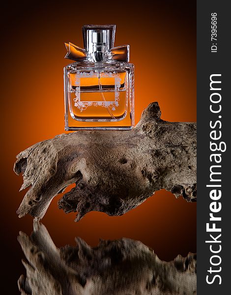 Still life view of luxurious perfume bottle on lump of wood, reflecting on orange tinted background.