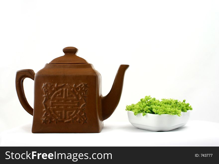 Small square brown teapot witch chinese pattern opposite to green flowers put in white porcelain. Small square brown teapot witch chinese pattern opposite to green flowers put in white porcelain