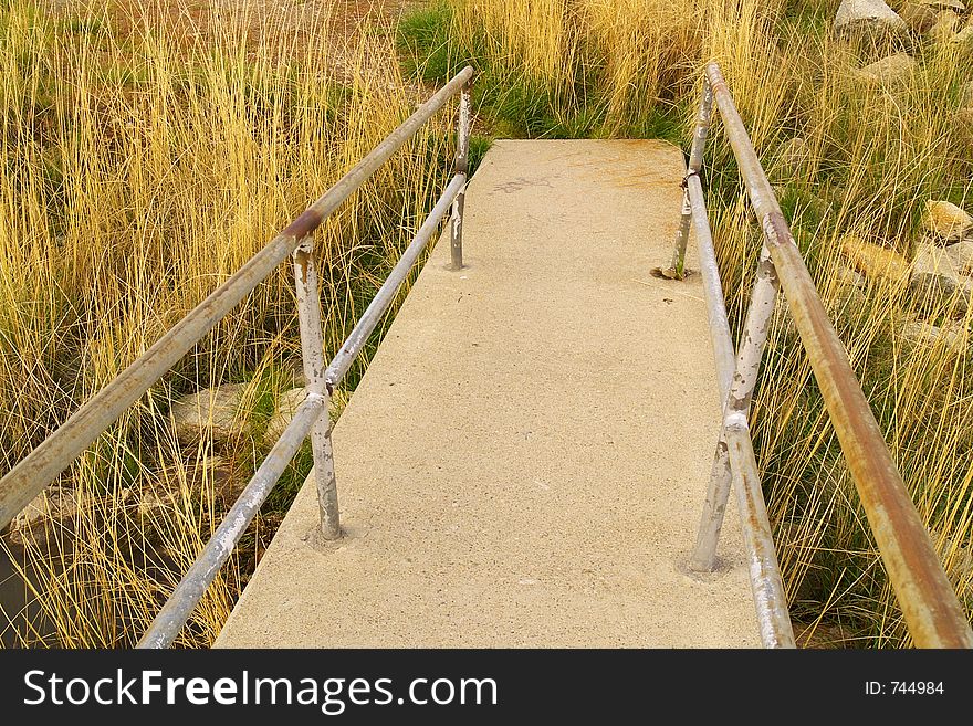 Concrete sidewalk with steel railing leading into grass and badlands.