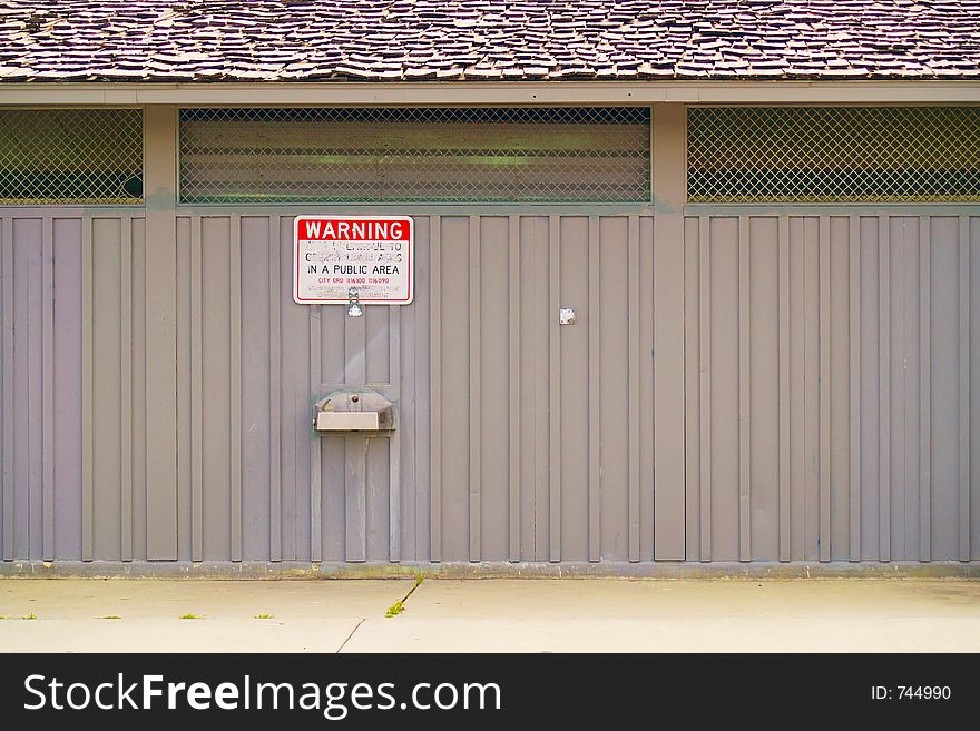 Water fountain on the side of a prefabricated steel building under a defaced or vandalized sign in a public urban area. Water fountain on the side of a prefabricated steel building under a defaced or vandalized sign in a public urban area.