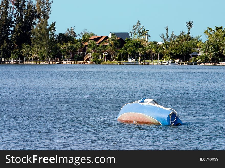 Sunken and abandoned sailboat backdropped with impressive waterfront homes. Sunken and abandoned sailboat backdropped with impressive waterfront homes