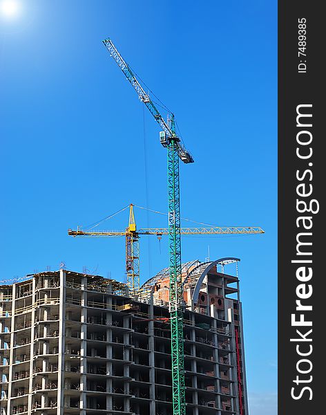Unfinished building with cranes on blue sky background