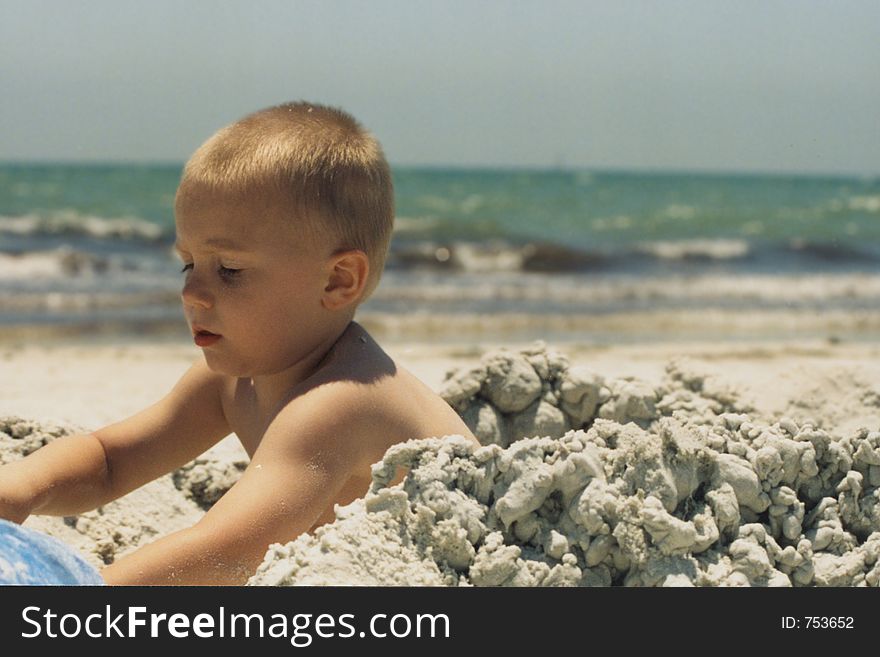 Toddler (boy) playing in the sand at the beach, build a sand castle. Toddler (boy) playing in the sand at the beach, build a sand castle