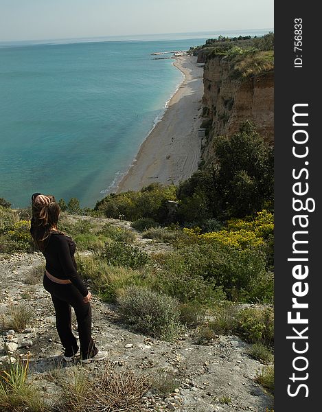 Young attractive female stands on a cliff relaxing a enjoying her view of the Adriatic Sea and Fontana de la Rosa from Gargano National Park in Southern Italy. Young attractive female stands on a cliff relaxing a enjoying her view of the Adriatic Sea and Fontana de la Rosa from Gargano National Park in Southern Italy