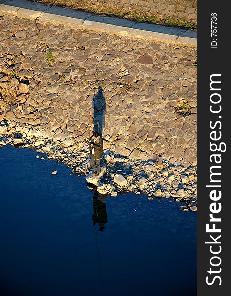 A man fishing on a bank of a river. A man fishing on a bank of a river