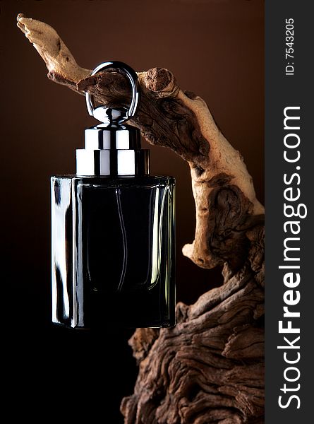 A black designer perfume bottle hung on a wooden branch. A black designer perfume bottle hung on a wooden branch.