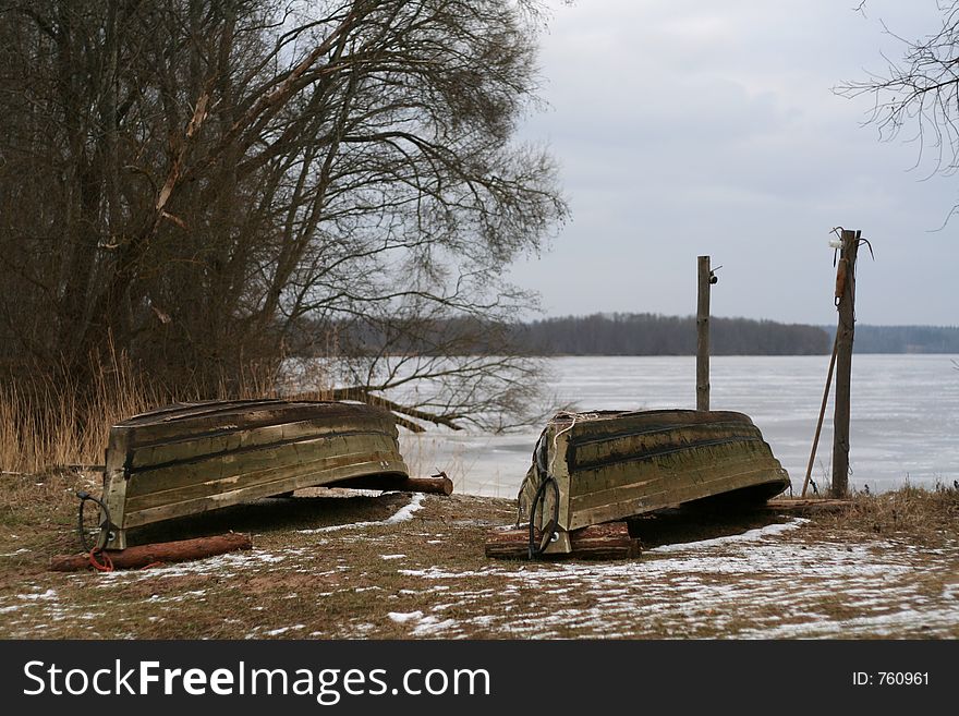 Two boats lying upside-down on frozen lake's shore