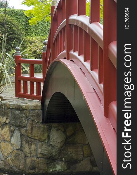 Angled view of a red arched bridge in a garden. Angled view of a red arched bridge in a garden