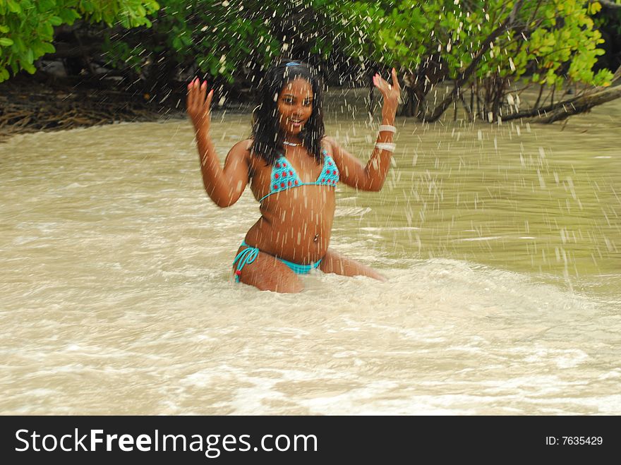 Island girl in bikini splashing water from ocean on seashore