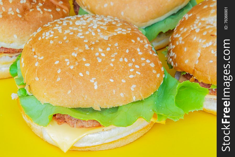 Picture with delicious beef hamburger with salad and cheese on a yellow plate. Picture with delicious beef hamburger with salad and cheese on a yellow plate