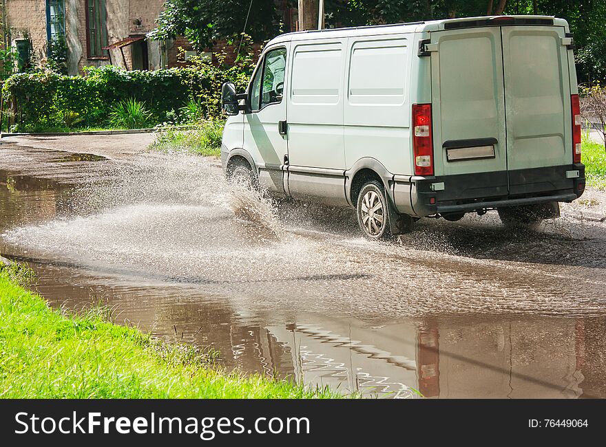 White commercial vehicle riding on big puddle on the road in residental area on summer day. White commercial vehicle riding on big puddle on the road in residental area on summer day