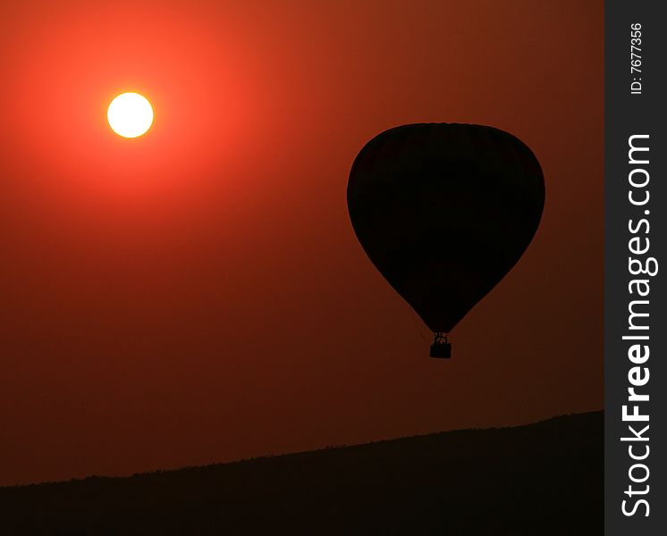 Hot-air balloon floating over a mountain with the sunset in the background. Hot-air balloon floating over a mountain with the sunset in the background