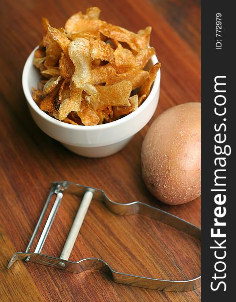 Crispy home-made french fries or potato chips served in a white ceramic bowl, striped napkin on wooden chopping block.