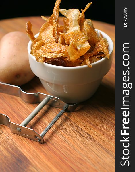 Crispy home-made french fries or potato chips served in a white ceramic bowl, on wooden chopping block with peeler and potato. Crispy home-made french fries or potato chips served in a white ceramic bowl, on wooden chopping block with peeler and potato.