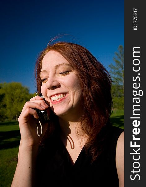 A pretty young woman enjoys a conversation on her cellular phone outdoors. A pretty young woman enjoys a conversation on her cellular phone outdoors.