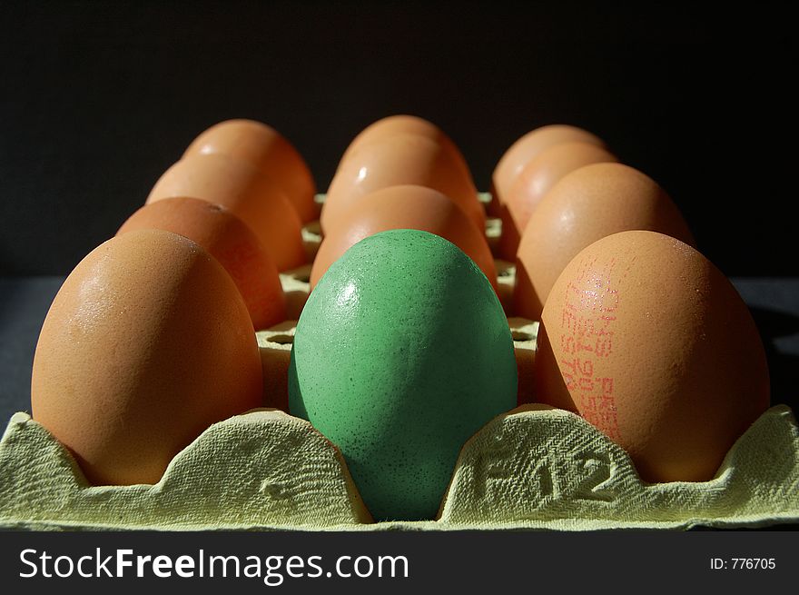 Green egg amongst normal eggs on black background. Green egg amongst normal eggs on black background