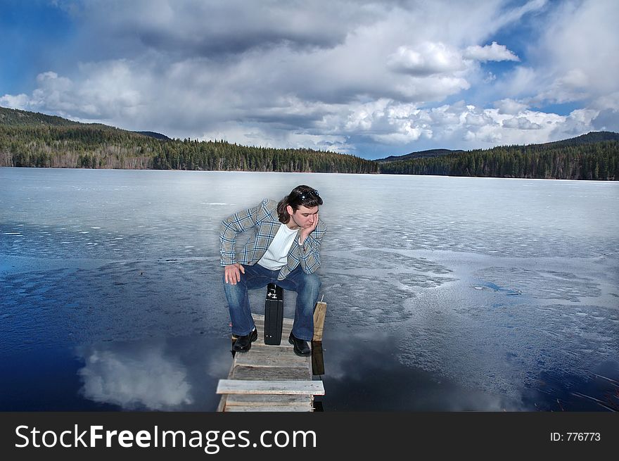 Sad looking businessman sitting on his briefcase and thinking, outdoors on a frozen lake.