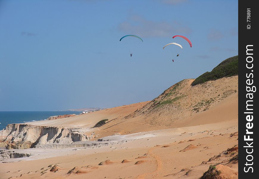 Paragliders fly over a white sand dune. Paragliders fly over a white sand dune.