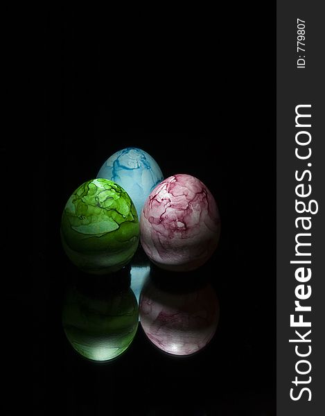 Three colored eggs on black with mirror reflection