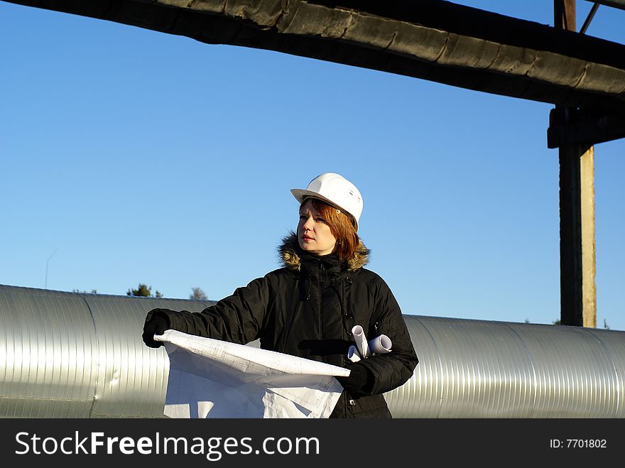 Young architect looking at blueprint in front of construction site against blue sky