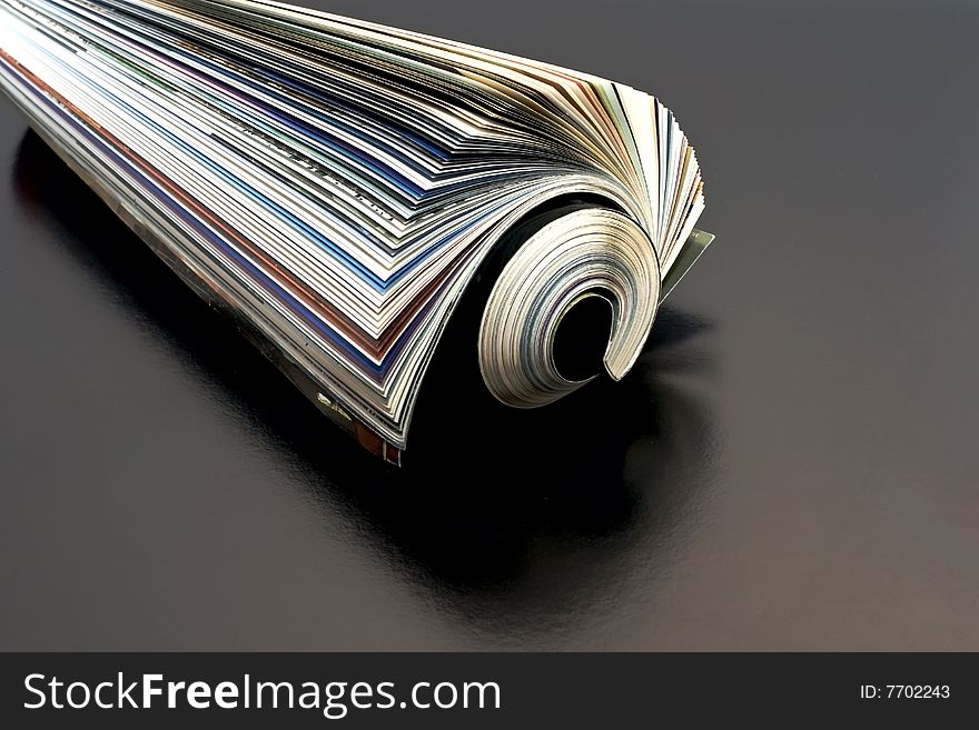 Newspaper rolled up dark background isolate.