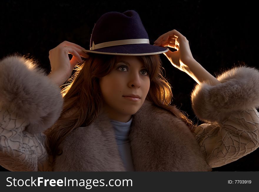 Young lady tryimg on a hat, on a black background