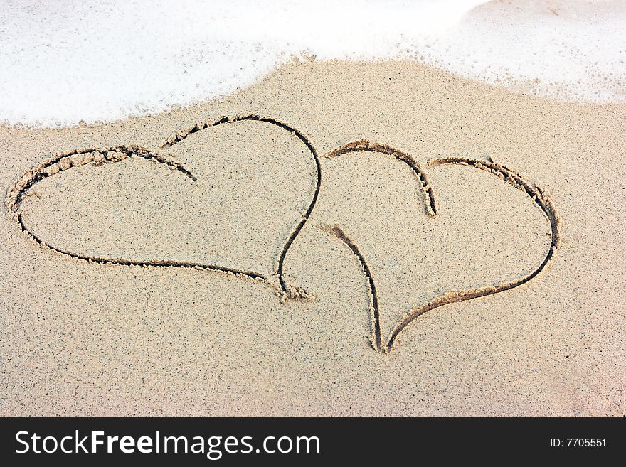 Two hearts drawing on the sandy beach