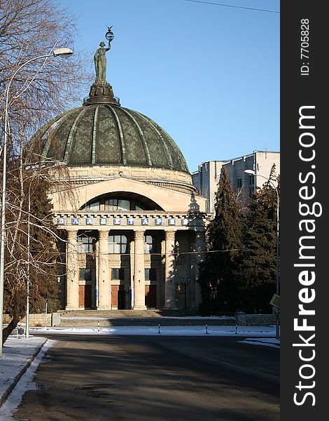 Building of a planetarium with a dome and a statue above on a background of the dark blue sky