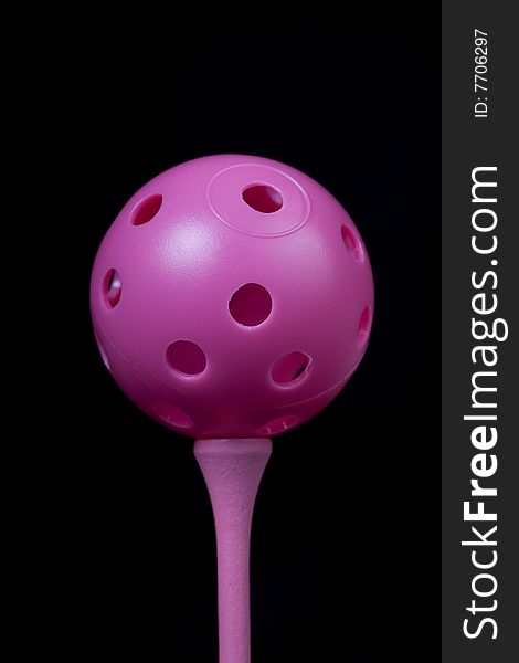 Pink practice ball on golf tee with black background. Pink practice ball on golf tee with black background
