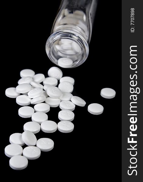 Details of small white pills spilling out of medicine container, isolated on black background. Details of small white pills spilling out of medicine container, isolated on black background