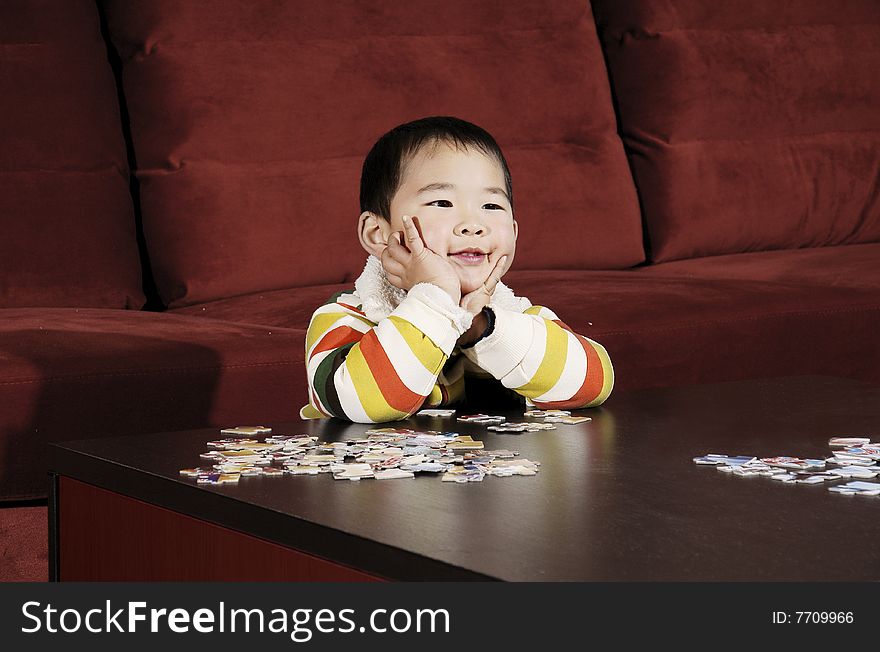 A picture of a chinese little boy thinking and smiling while playing jigsaw puzzle. A picture of a chinese little boy thinking and smiling while playing jigsaw puzzle