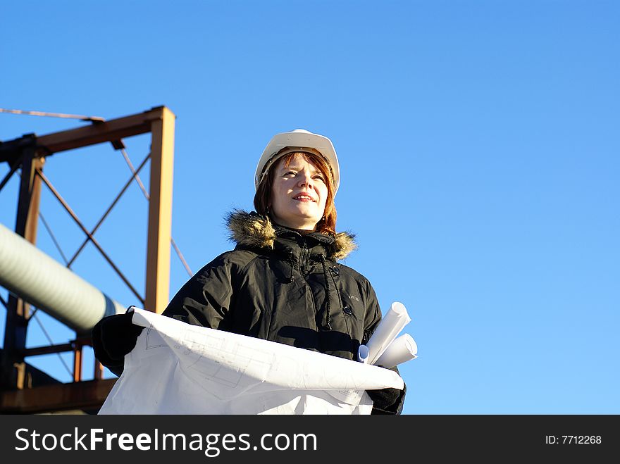 Young architect looking at blueprint in front of construction site against blue sky