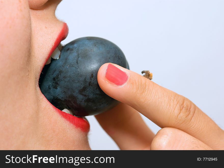 Girl, holding a plum between her teeth, taking a bite. Girl, holding a plum between her teeth, taking a bite