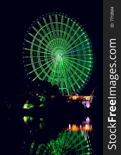 A ferris wheel with colour lights on at night and its reflection in water. A ferris wheel with colour lights on at night and its reflection in water