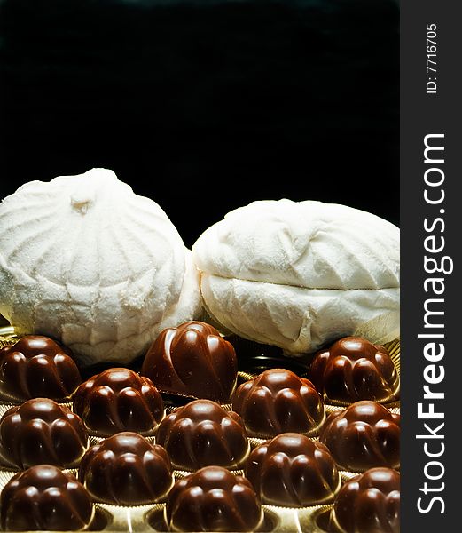 Chocolates and soft white marshmallows on a black background