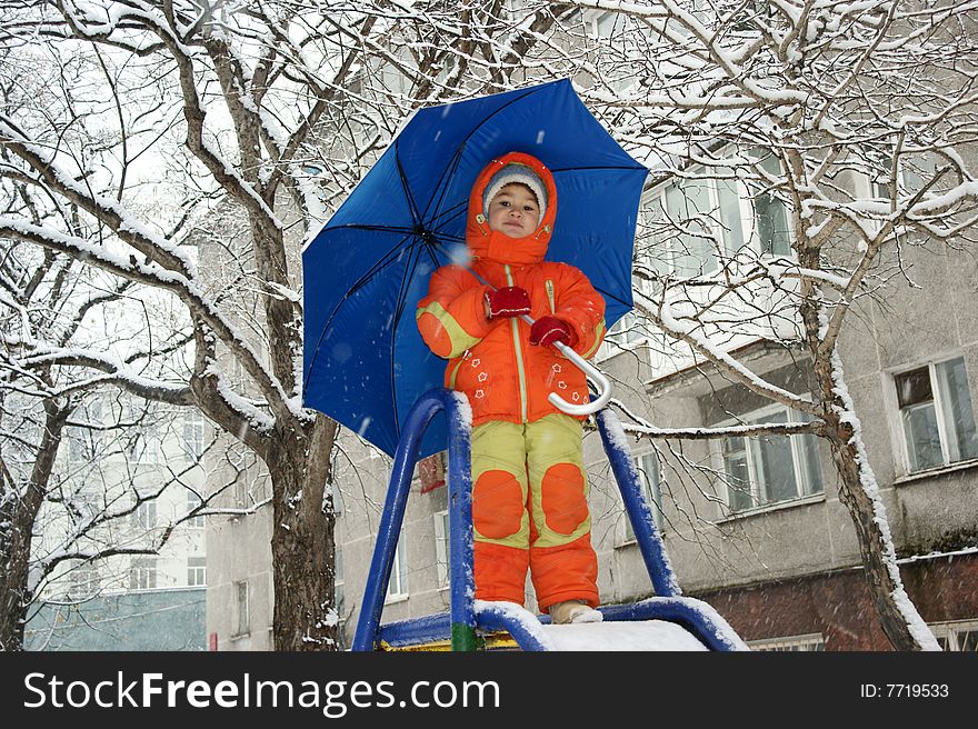 Child in red overalls on background of the blue umbrella