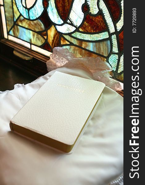 White bible on satin pillow with stained glass in background. White bible on satin pillow with stained glass in background