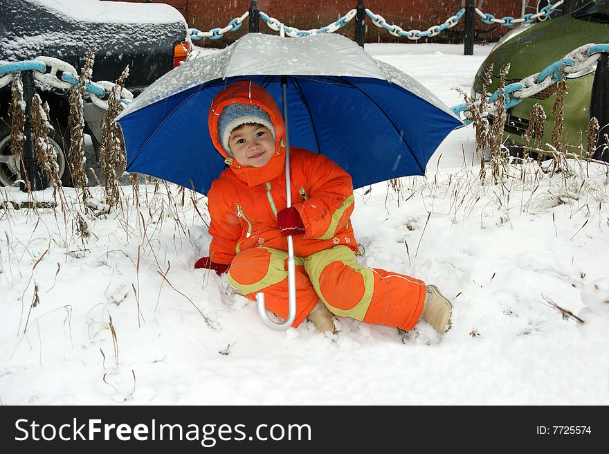 Child in red overalls on background of the blue umbrella