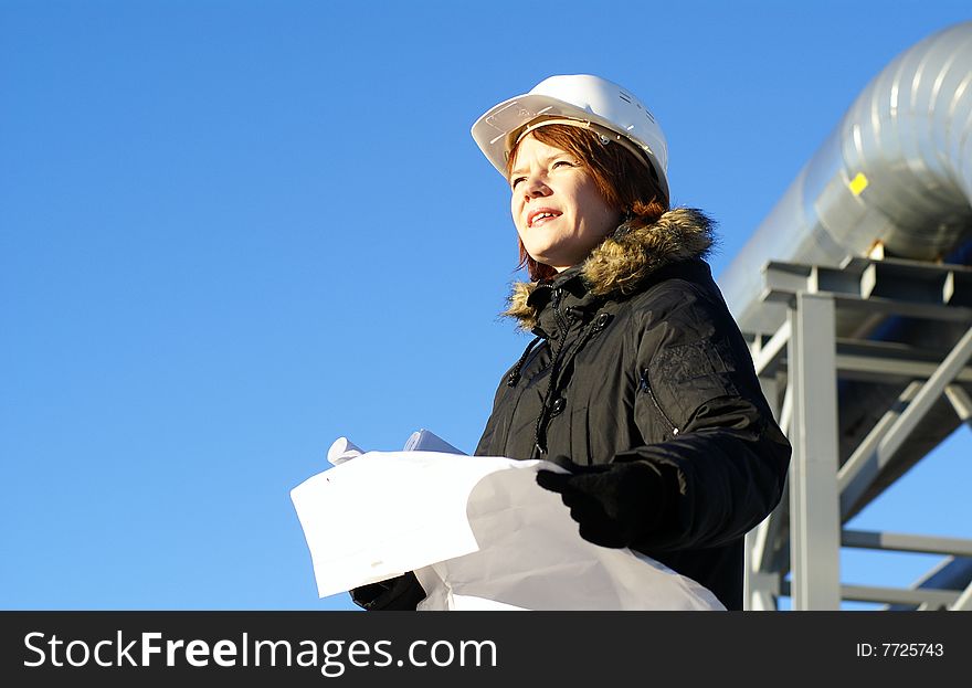 Young architect looking at blueprint in front of construction site against blue sky. Young architect looking at blueprint in front of construction site against blue sky