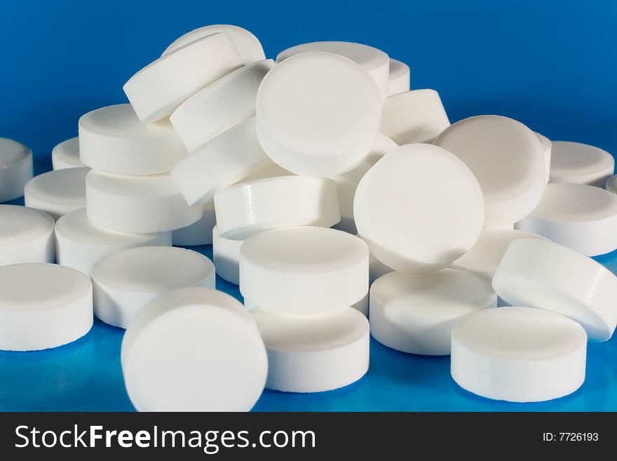 Closeup of a pile of white pills (on a bright blue background)