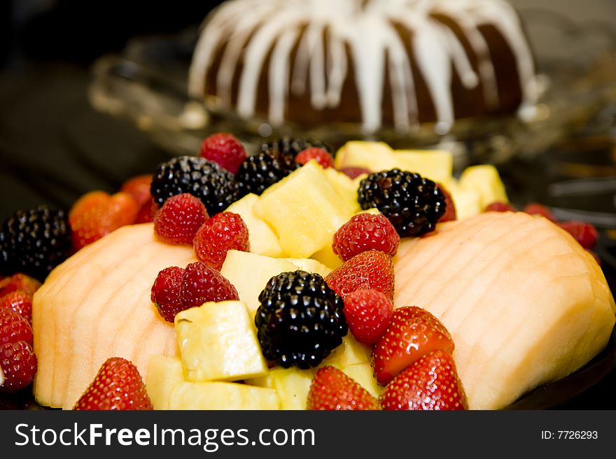 Fresh cut fruit and berries with a frosted cake in the background. Fresh cut fruit and berries with a frosted cake in the background