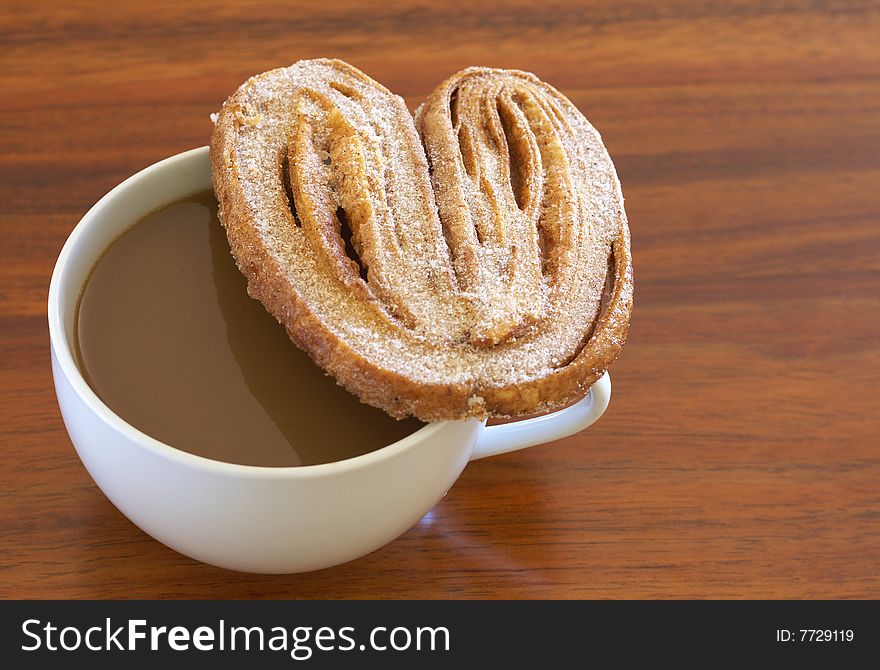 Cup of hot coffee and baked palmier cookie on wooden table background. Cup of hot coffee and baked palmier cookie on wooden table background