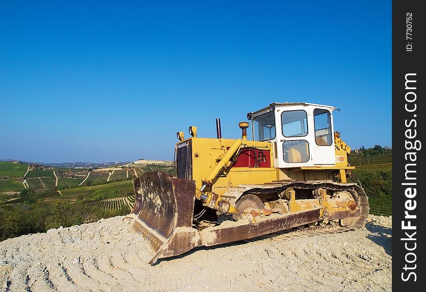 An excavator on the Langhe hills, full of green vineyards, Piedmont, Italy. An excavator on the Langhe hills, full of green vineyards, Piedmont, Italy.