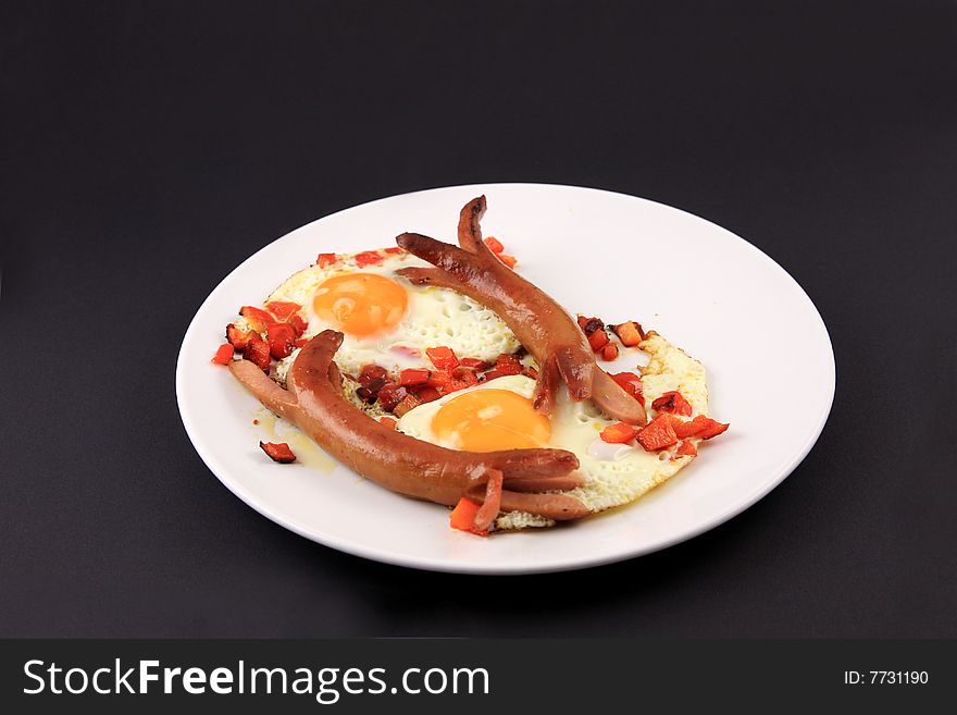 Fried eggs with sausages over black background