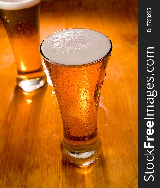 Two beer glasses on wood background, focus on first. Two beer glasses on wood background, focus on first