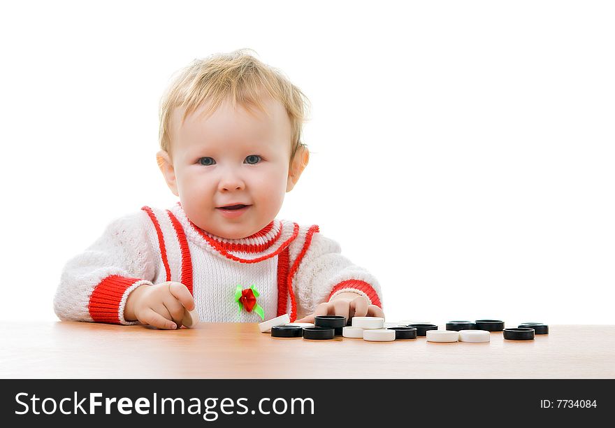 A little child sitting at a table with the heap of checkers lies on. A little child sitting at a table with the heap of checkers lies on