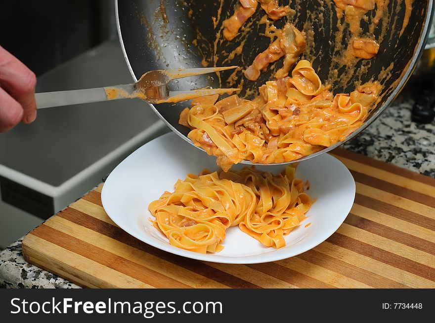 Pouring pasta using fork from pan into plate